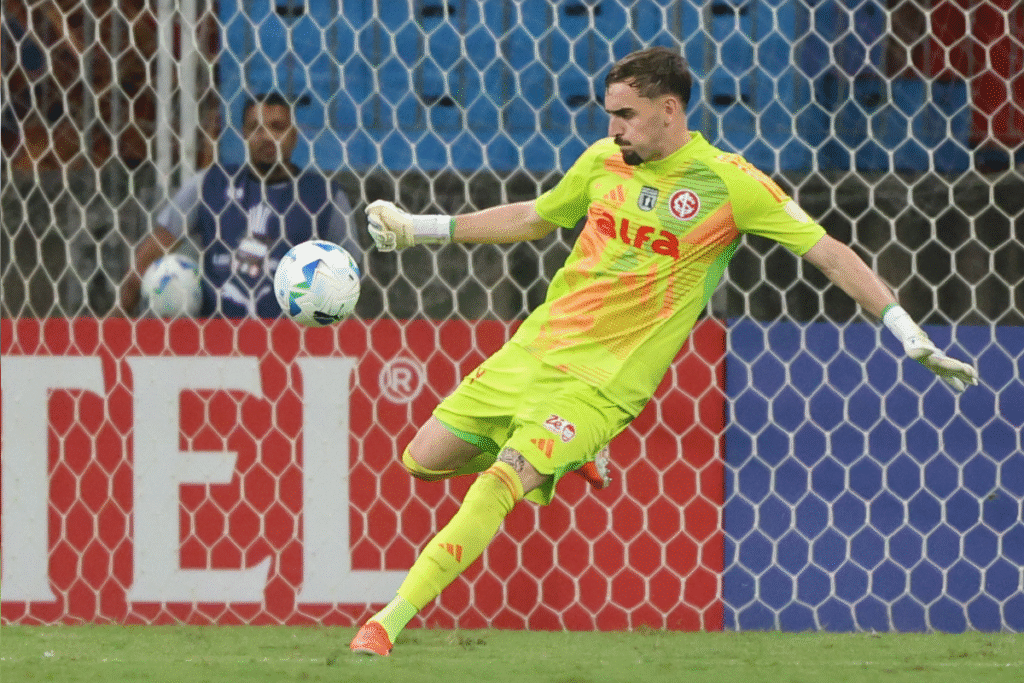 Goleiro do Internacional saltando para fazer defesa em partida com torcida vibrante